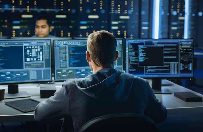 IT Specialist Works on Personal Computer with Screens Showing Software Program with Coding Language Interface. The image shows an IT professional working in a technical room of a data center.